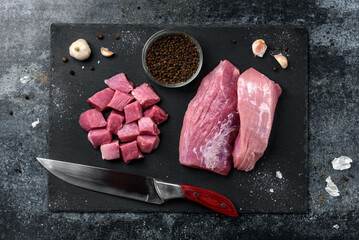 Diced raw pork meat with on slate board on black background.