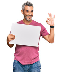 Middle age grey-haired man holding blank empty banner doing ok sign with fingers, smiling friendly gesturing excellent symbol