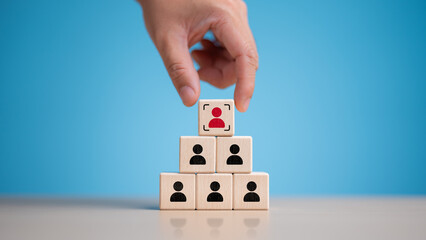 Hand pick red people icon on top of wooden cube. Human resources management and business hire recruitment. Corporate hierarchy, recruiting for team by professional person, Headhunter or staff search.