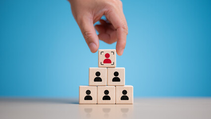 Hand pick red people icon on top of wooden cube. Human resources management and business hire...