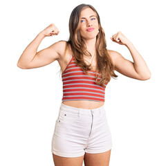 Beautiful caucasian young woman wearing casual clothes showing arms muscles smiling proud. fitness concept.