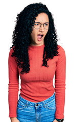 Young hispanic woman with curly hair wearing glasses angry and mad screaming frustrated and furious, shouting with anger. rage and aggressive concept.