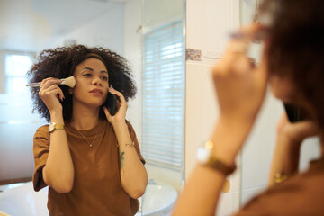 Hispanic woman talking on phone with friend and applying makeup