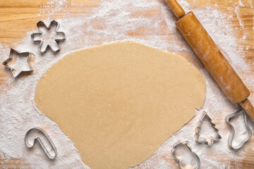 An overhead view of dough rolled out for Christmas theme cookies on a wooden butcherblock with flour and a wooden rolling pin.