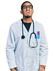 Young african american man wearing doctor uniform and stethoscope angry and mad screaming frustrated and furious, shouting with anger. rage and aggressive concept.