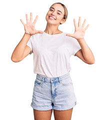 Young beautiful blonde woman wearing casual white tshirt showing and pointing up with fingers number ten while smiling confident and happy.