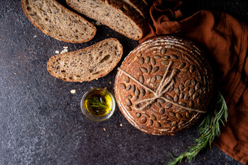 Obraz premium Sliced sourdough bread from whole grain flour and pumpkin seeds on a grid, olive oil and black olive on a rustic wooden table. Artisan bread.
