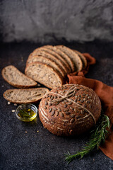 Sliced sourdough bread from whole grain flour and pumpkin seeds on a grid, olive oil and black olive on a rustic wooden table. Artisan bread.