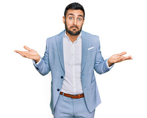Young hispanic man wearing business jacket clueless and confused expression with arms and hands raised. doubt concept. - obrazy, fototapety, plakaty