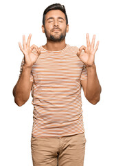 Handsome hispanic man wearing casual clothes relaxed and smiling with eyes closed doing meditation gesture with fingers. yoga concept.