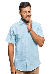 Handsome hispanic man wearing casual clothes touching mouth with hand with painful expression because of toothache or dental illness on teeth. dentist