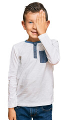 Adorable caucasian kid wearing casual clothes covering one eye with hand, confident smile on face and surprise emotion.