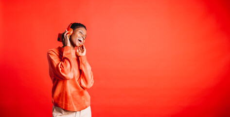 Happy young woman dancing and singing while wearing wireless headphones in a studio. Woman...