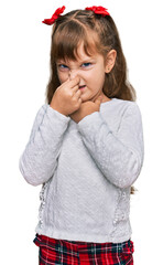 Little caucasian girl kid wearing casual clothes smelling something stinky and disgusting, intolerable smell, holding breath with fingers on nose. bad smell