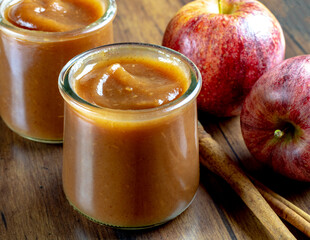Jars of homemade sweet apple butter with cinnamon sticks and apples.