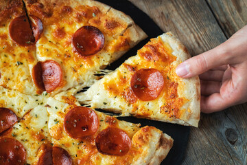 A slice of hot Italian pizza with stretching cheese. Pizza pepperoni on a dark wooden background