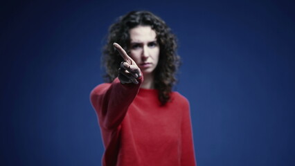 Young Woman Firmly Saying NO to Camera, 20s Woman Rejecting with Crossed Arms and Finger Wave, standing on blue backdrop