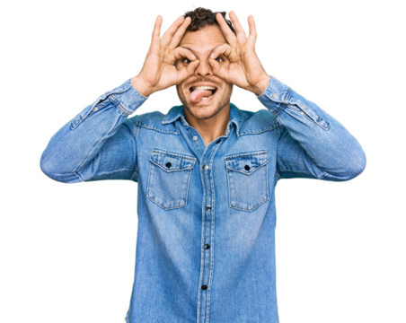 Young hispanic man wearing casual denim jacket doing ok gesture like binoculars sticking tongue out, eyes looking through fingers. crazy expression.