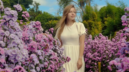 Young woman in white dress walks through blooming violet wildflowers field on sunny spring day. Floral background, beautiful nature, fresh air, beauty concept.