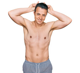 Fototapeta premium Handsome young man wearing swimwear shirtless posing funny and crazy with fingers on head as bunny ears, smiling cheerful