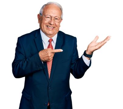 Senior man with grey hair wearing business suit and glasses amazed and smiling to the camera while presenting with hand and pointing with finger.