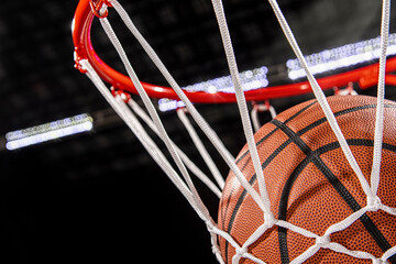 A close-up view of a basketball falling through the rim and nylon net with the arena lights in the...