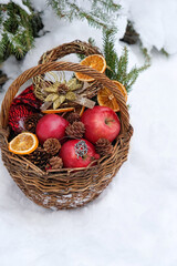 wicker basket with apples, pentacle amulet, decorations, mittens, cones in snowy forest. Winter...