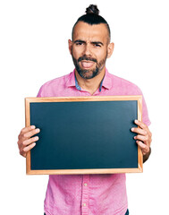 Hispanic man with ponytail holding blackboard sticking tongue out happy with funny expression.