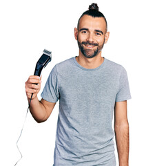 Hispanic man with ponytail holding electric razor machine looking positive and happy standing and...