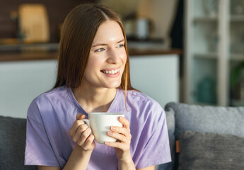 Beautiful happy woman relaxes at home, surrounded by warmth and domestic comfort, savoring hot tea or coffee. Tranquility and Comfort concept