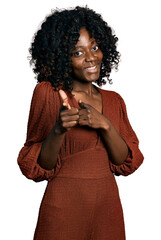 Fototapeta na wymiar African woman with curly hair wearing casual dress pointing fingers to camera with happy and funny face. good energy and vibes.