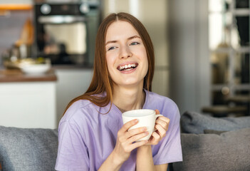 Happy smiling woman woman in a cozy interior, relaxes at home, surrounded by warmth and domestic comfort, savoring hot tea or coffee. Tranquility and Comfort concept