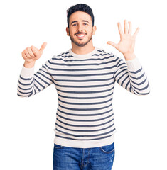 Fototapeta premium Young hispanic man wearing casual clothes showing and pointing up with fingers number six while smiling confident and happy.