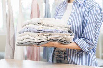 Feel softness, chore of pretty asian young woman hand holding pile clothing from table, stack folding clean clothes after washing, laundry and dry. Household working at home. Laundry of maid concept. - obrazy, fototapety, plakaty