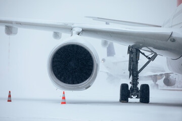 Traffic at airport during heavy snowfall. Snowflakes against jet engine and taxiing airplane at airport taxiway during frosty winter day. Extreme weather in transportation..