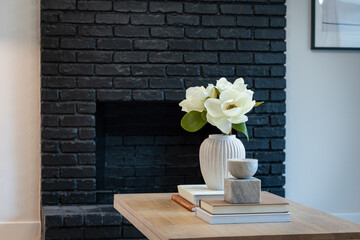 Simple living room detail of black painted brick fireplace with light wood coffee table and vase of flowers.