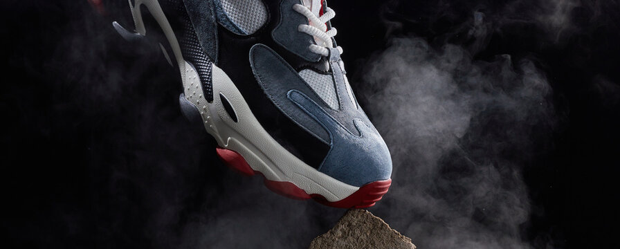 Sneakers and smoke on dark background. Modern shoe for walking. Shoes on stone platform.