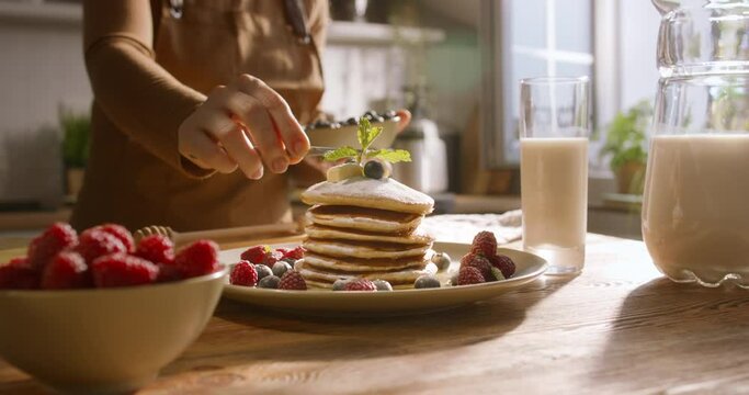 Unrecognizable chef decorates pancakes with sprig of mint. Advertising cinematic. Excess sugar dangerous, diabetes-friendly offerings. Guilt-free cheat meal, perfect balance between taste and wellness