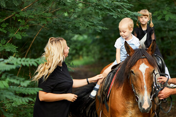 A happy mother. Daughter and little son are having fun riding horses. A girl and her children are...