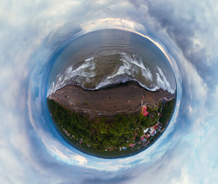 Little planet view of the beach with black magnetic sands in Georgia. Storm waves, garbage on the Ureki beach after bad weather, no swimming. Danger on the water for vacationers. Cumulonimbus.