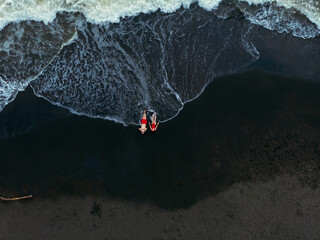 Black sand beach. Fantastic landscape of black sand volcano Ureki beach in Georgia. Couple having a good time on vacation. A man and a woman in red swimsuits are lying down - obrazy, fototapety, plakaty