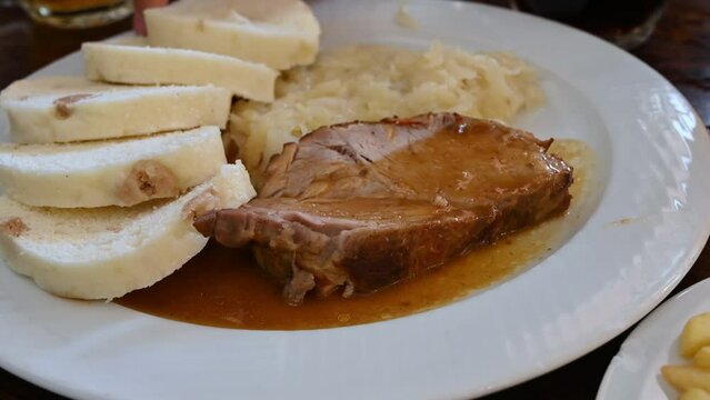 Prague, Czech Republic, August 4,2023. Close-up with one of the typical dishes: stewed pork with sauerkraut and bread for dipping. A side dish of chips, mugs of light and dark beer. The hand grabs