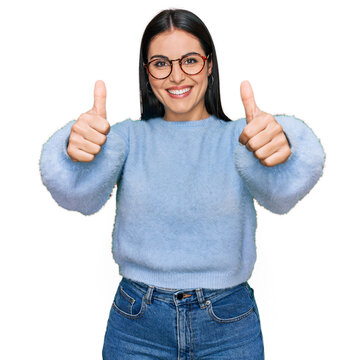 Young hispanic woman wearing casual clothes and glasses approving doing positive gesture with hand, thumbs up smiling and happy for success. winner gesture.