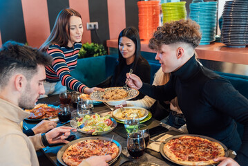 Group of friends having dinner with pizza and pasta in restaurant