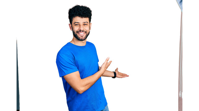 Young arab man with beard wearing casual blue t shirt inviting to enter smiling natural with open hand
