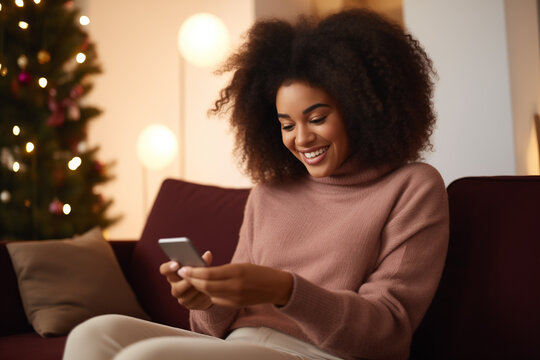 Happy relaxed young woman sitting on couch using cell phone, Christmas time. Smiling lady holding smartphone. Looking at cell phone enjoying doing online e commerce shopping in mobile apps