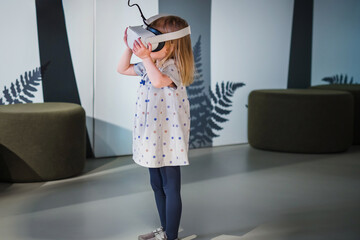 Adorable toddler girl with a virtual reality headset standing in a natural history museum playroom....
