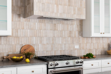 A kitchen oven and hood detail with brown rectangle tiles, stainless steel oven, white cabinets,...
