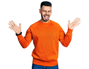 Young hispanic man with beard wearing casual orange sweater celebrating mad and crazy for success...