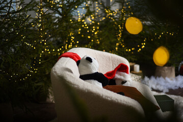 Christmas interior with a white sofa near green Christmas trees with lights that create a bokeh effect. two soft toy pandas with a red gnome hat on a white sofa.